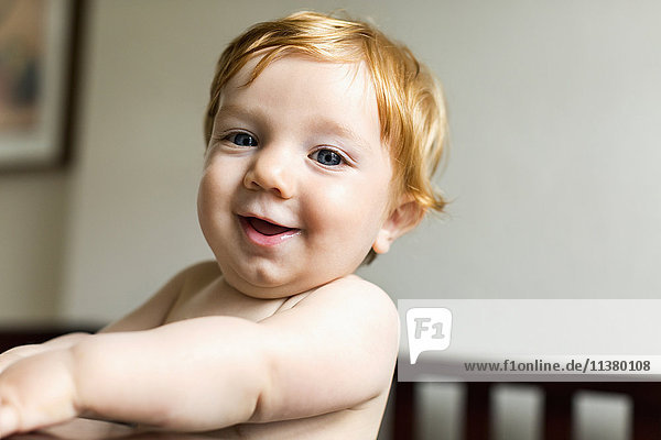 Portrait of smiling Caucasian baby boy standing in crib
