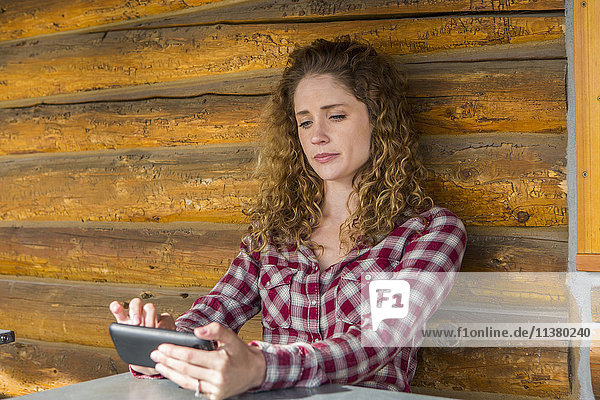Caucasian woman leaning on wooden wall texting on cell phone