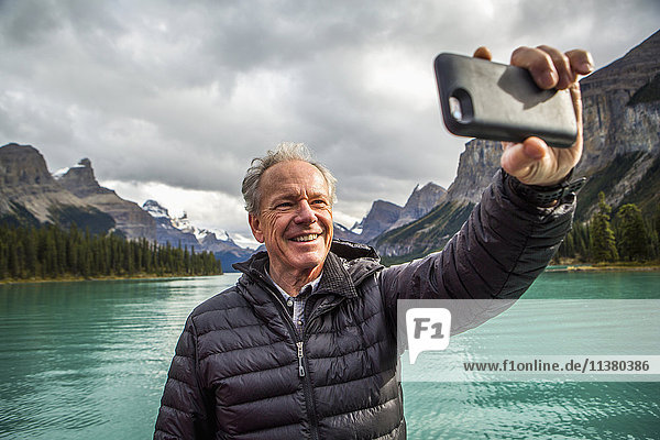 Caucasian man posing for cell phone selfie near mountain lake