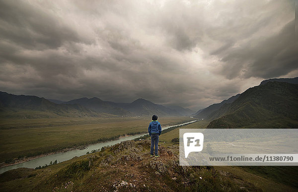 Kaukasischer Junge in der Nähe eines Flusses in einer bewölkten Landschaft stehend