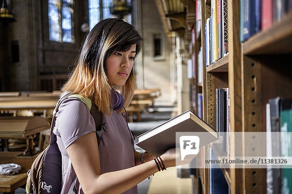 Chinesische Frau steht in der Bibliothek und liest ein Buch