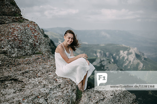 Lächelnde kaukasische Frau sitzt auf einem Felsen mit Blick auf die Landschaft