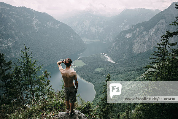 Kaukasischer Mann steht auf einem Felsen mit Blick auf einen See im Tal