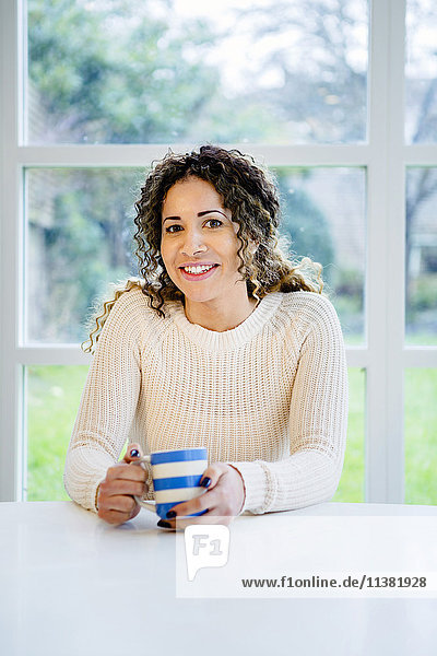 Lächelnde Frau sitzt am Tisch und hält eine Kaffeetasse