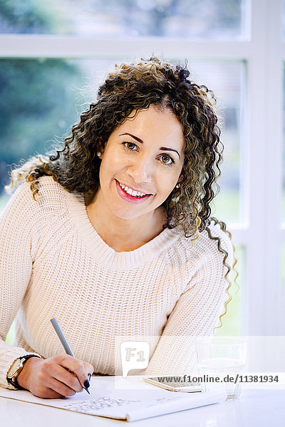 Smiling woman sitting at table writing on notepad with pen