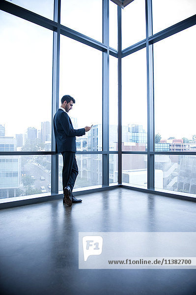 Hispanischer Geschäftsmann lehnt am Fenster und schreibt eine SMS mit seinem Handy