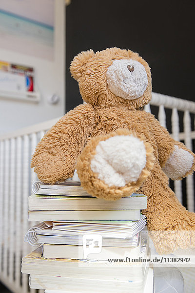 Teddybär auf Bücherstapel neben Krippe