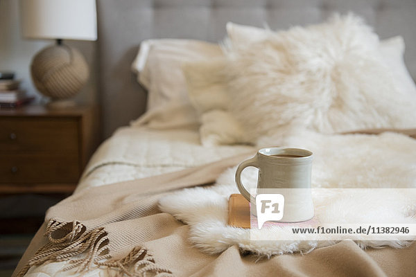 Coffee cup and book on fur on bed