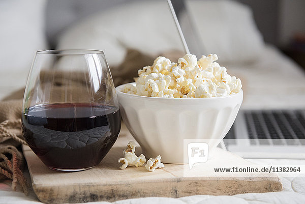 Eine Schüssel Popcorn und ein Glas Wein neben dem Laptop