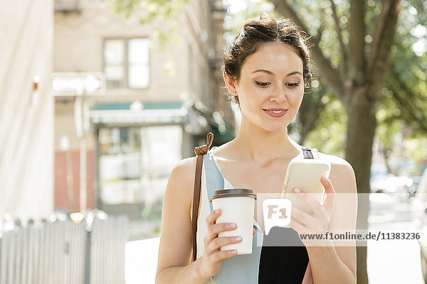 Thai woman holding coffee texting on cell phone in city