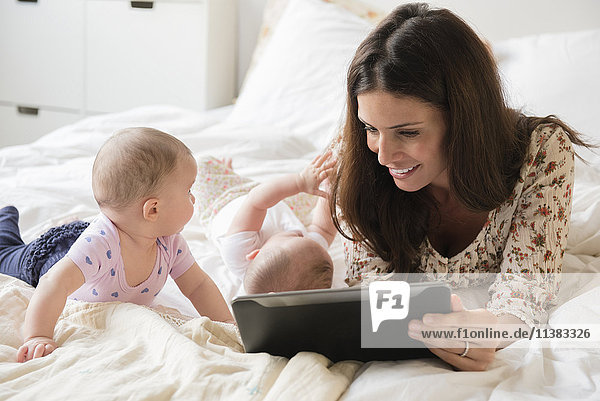 Kaukasische Mutter auf dem Bett mit Zwillingsbaby Töchter mit digitalem Tablet