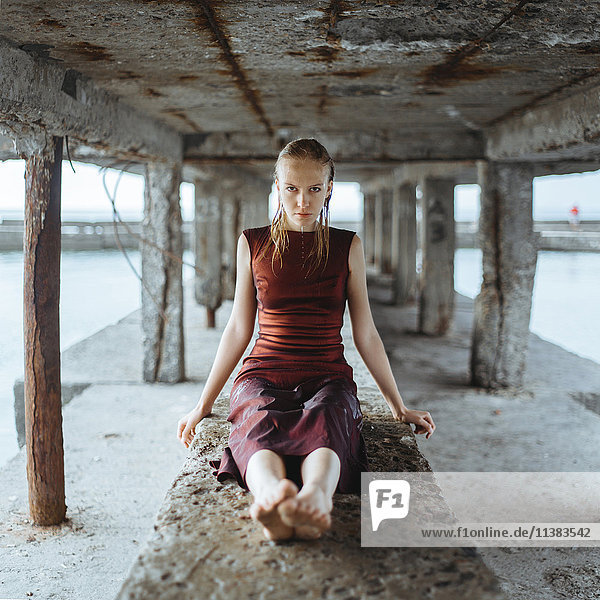 Kaukasisches Mädchen mit nassem Kleid  das unter einem Dock sitzt