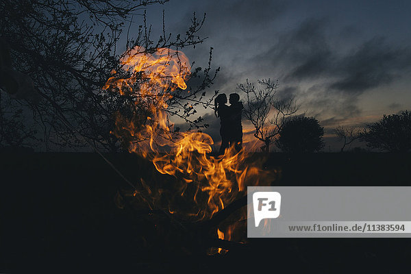 Silhouette eines kaukasischen Paares  das sich in der Nähe des Feuers küsst
