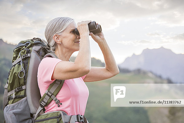 Kaukasische Frau wandert auf einem Berg und benutzt ein Fernglas