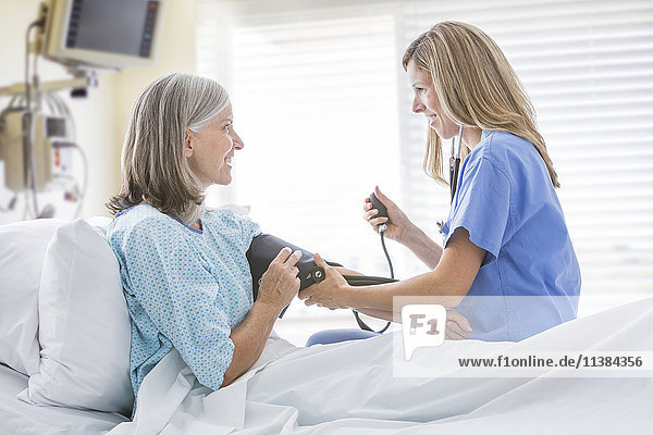 Kaukasische Krankenschwester misst den Blutdruck einer Frau im Krankenhausbett