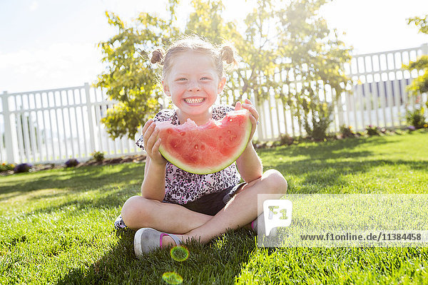Caucasian girl sitting in grass eating watermelon
