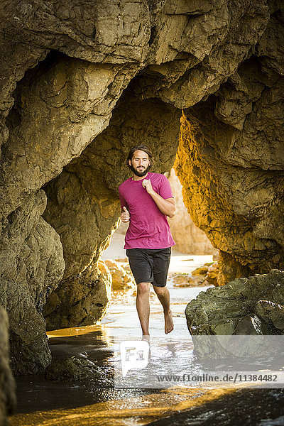 Caucasian man running under rock formation at beach