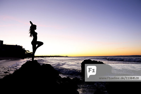 Silhouette of Caucasian woman balancing on rock at beach