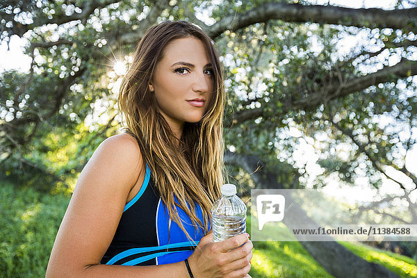 Caucasian woman holding water bottle near tree