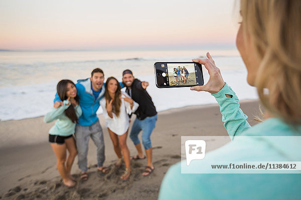 Frau fotografiert Freunde am Strand mit Mobiltelefon