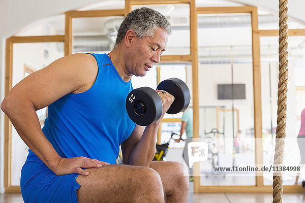Mixed Race man curling dumbbell in gymnasium