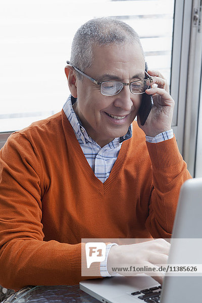 Lächelnder hispanischer Mann beim Multitasking mit Handy und Laptop