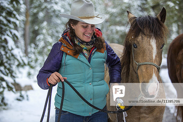Lächelnde kaukasische Frau hält die Zügel ihres Pferdes im Winter