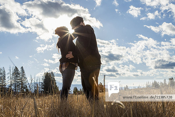Kaukasisches Paar küsst sich in einem sonnigen Feld