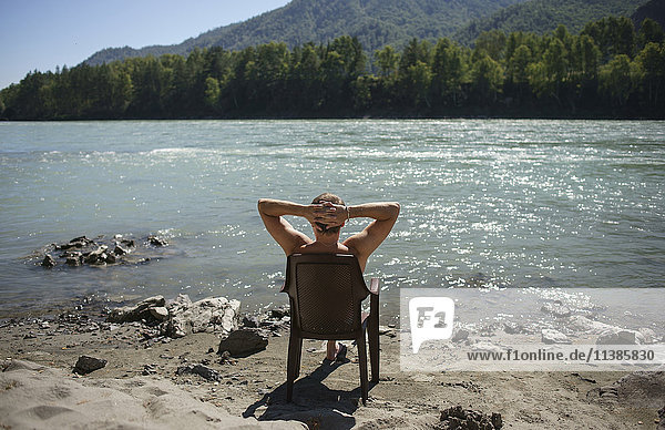 Kaukasischer Mann sitzt im Stuhl und sonnt sich in der Nähe des Flusses