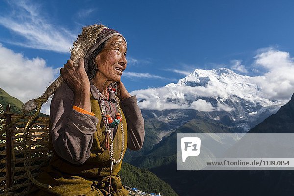 Bäuerin  die einen Korb mit geernteten Pflanzen trägt  mit dem Mount Annapurna II in der Ferne  Ghyaru  Bezirk Manang  Nepal  Asien