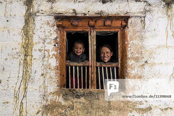 Junge Frau und Sohn schauen aus Fenster des Bauernhof Purang Mustang Nepal Asien