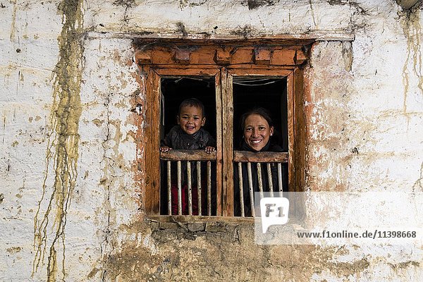 Junge Frau und Sohn schauen aus dem Fenster eines Bauernhauses  Purang  Bezirk Mustang  Nepal  Asien