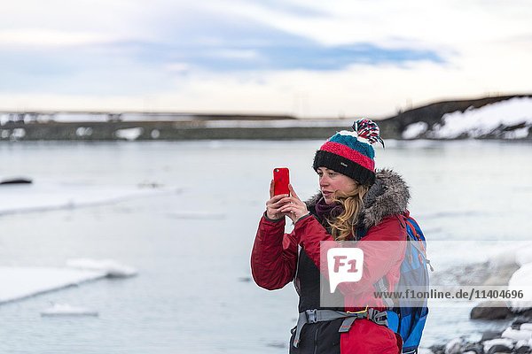Young woman taking photo with mobile phone  Fjallsárlón Glacier Lagoon  Iceland  Europe