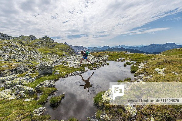 Wanderer springt über kleinen Bergsee mit Alpenpanorama  Schladminger Tauern  Schladming  Steiermark  Österreich  Europa