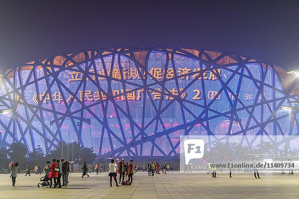 Menschen auf dem Platz vor dem beleuchteten Nationalstadion im Olympiapark  Dämmerung  Peking  China  Asien