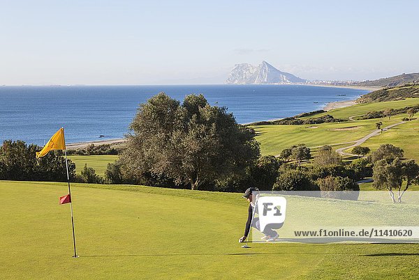 Golfer on putting green  La Alcaidesa Golf Resort with Mediterranean Sea and Rock of Gibraltar  Cádiz  Andalusia  Spain  Europe