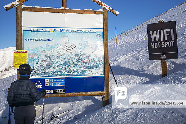 'A skier stands looking at a map of the Sunshine Village ski resort with a wifi hot spot sign beside it  Banff National park; Banff  Alberta  Canada'