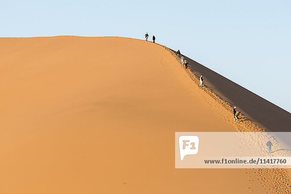 Touristen klettern am Rand einer riesigen Sanddüne in der Namib-Wüste; Namibia'.