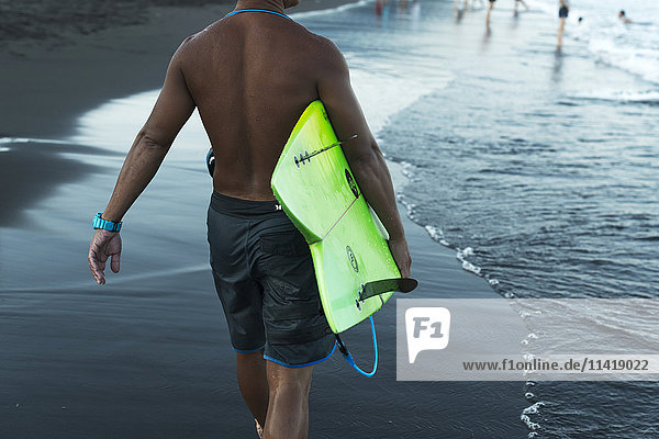 Ein männlicher Surfer trägt sein Surfbrett am Strand entlang  Waiao-Strand  Bezirk Yilan; Yilan  Taiwan  China'.