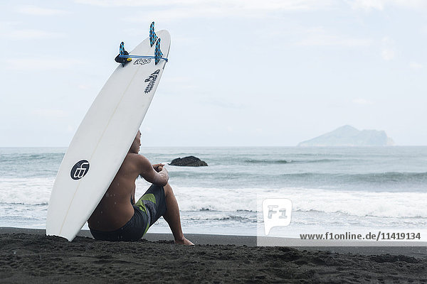 'A surfer sits on the shore as he waits to get into the sea Waiao beach Yilan County; Taiwan China'