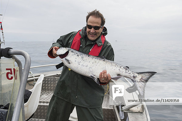 Ein Mann steht auf einem Fischkutter und hält einen frisch gefangenen großen Königslachs in der Hand; Queen Charlotte Islands  British Columbia  Kanada'.