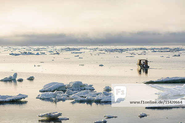 A small outboard boat motors through icebergs in the Arctic Ocean on a calm evening North Slope Barrow Arctic Alaska USA Summer