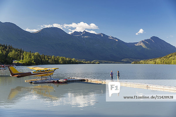 A woman and a man stand on a dock where a float plane is docked  Trail Lake Float Plane Base  Moose Pass  Kenai Peninsula  Southcentral Alaska  USA