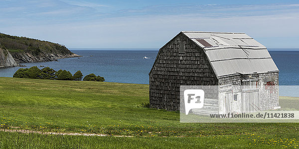 'A worn wooden building on a grass hillside overlooking the ocean; Saint Margaret Village  Nova Scotia  Canada'