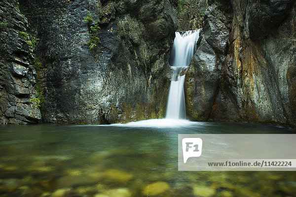 Ein doppelter Wasserfall fällt in grünes Wasser in einer dunklen Schlucht  Kananaskis Country; Alberta  Kanada'.
