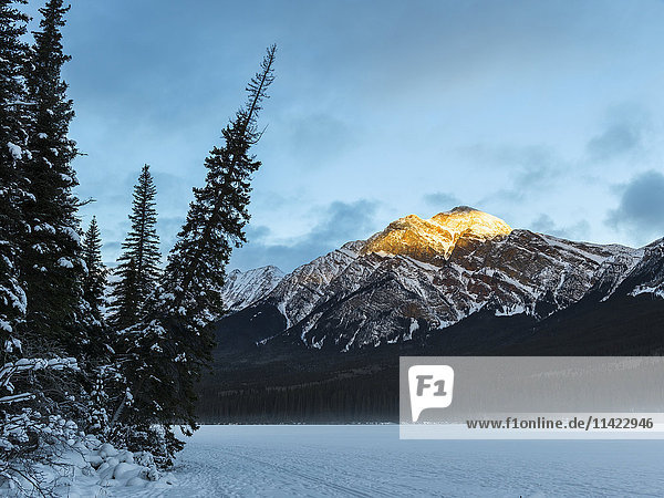 'Golden sunlight on the peak of a mountain with a frozen lake in the foreground  Jasper National Park; Jasper  Alberta  Canada'