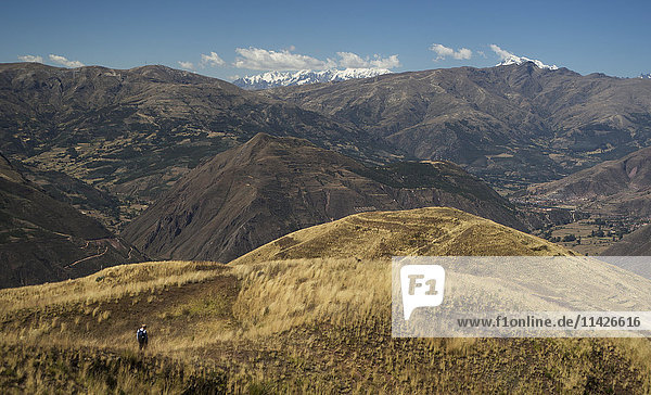 'A hiker makes his way through the foothills of the Andes Mountains with the snowcapped peaks in the background of the Peruvian landscape; Cusco Peru'