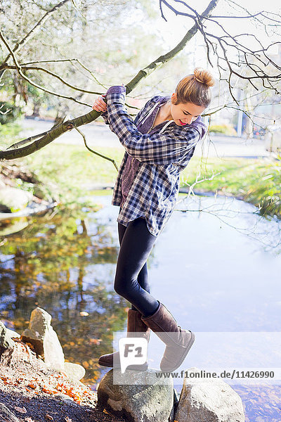 Ein junges Teenager-Mädchen unterhält sich lässig am Wasser  während sie einen Ast festhält; New Westminster  British Columbia  Kanada'.