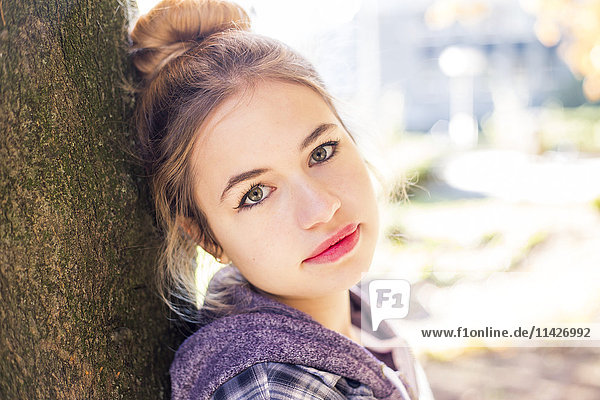Ein hübsches junges Mädchen im Teenageralter blickt mit schüchternem  unsicherem Blick in die Kamera  während sie sich an einen Baum lehnt; New Westminster  British Columbia  Kanada'.