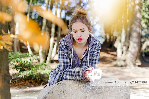Dieses junge Teenager-Mädchen sitzt allein in einem Park auf einem Felsen und denkt nachdenklich vor sich hin; New Westminster  British Columbia  Kanada